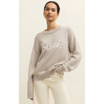 Load image into Gallery viewer, Woman wearing a beige sweater with 'beach' text on a plain background
