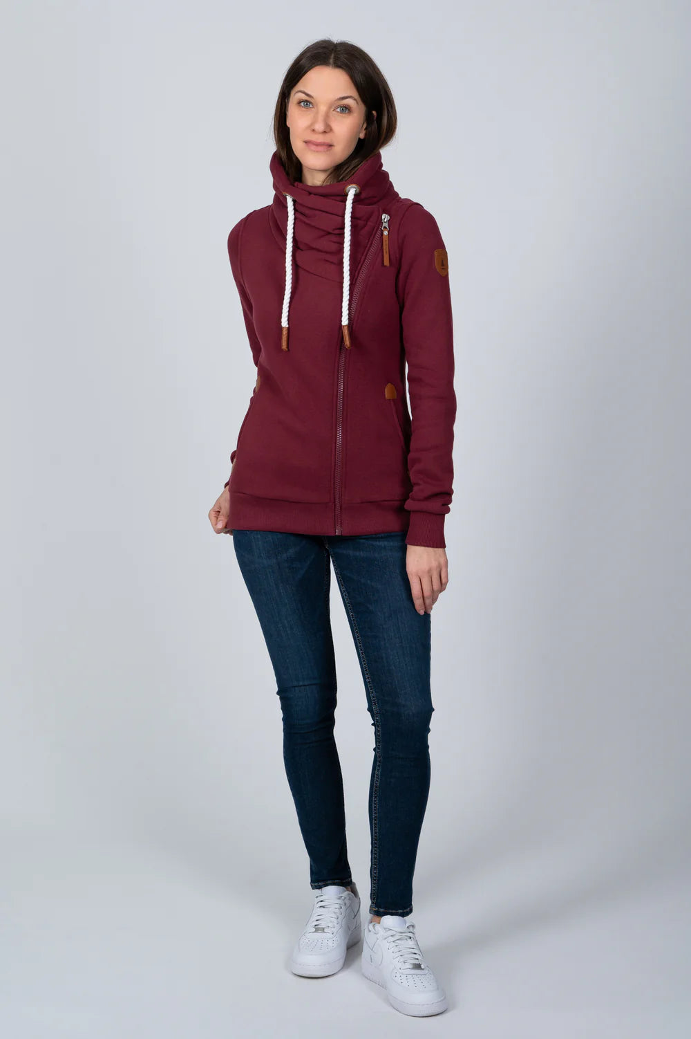 Woman wearing a burgundy sweatshirt with a high collar and blue jeans on a white background
