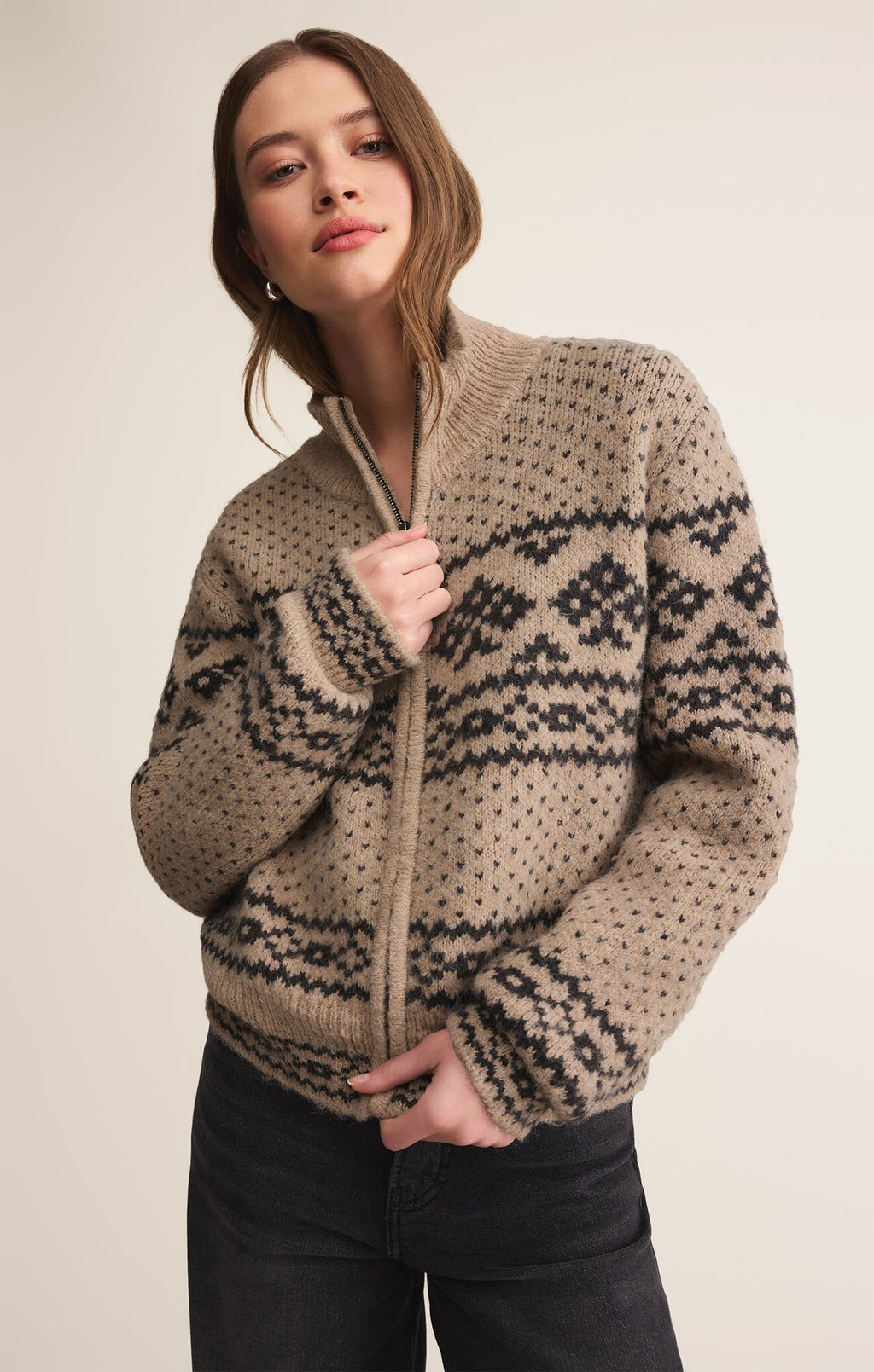 Woman wearing a beige zip up cardigan sweater with a geometric  pattern, standing against a plain background