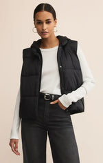 Load image into Gallery viewer, Woman wearing a black puffer vest over a white long-sleeve shirt on a beige background
