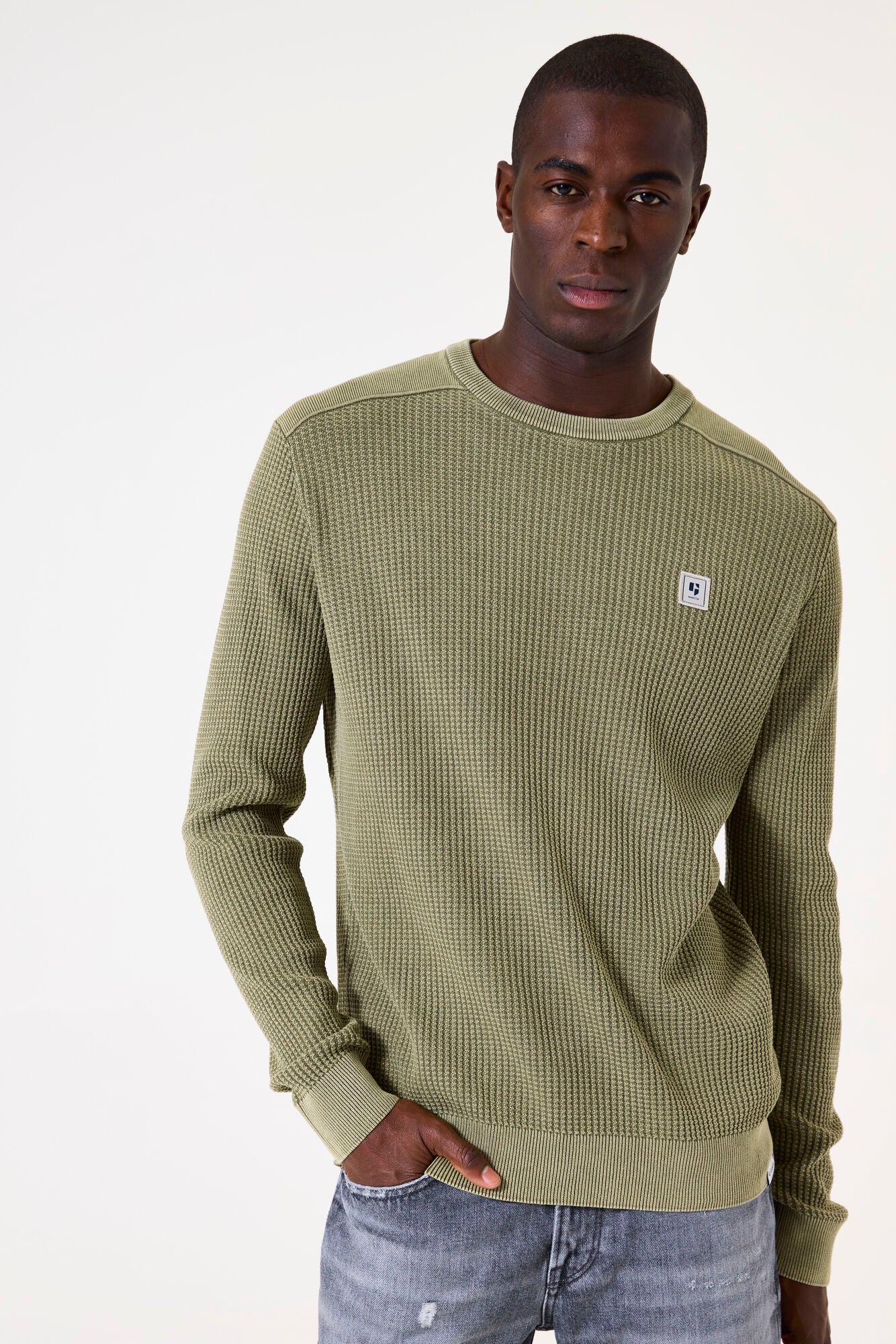 Man wearing a green textured sweater with a small logo on a white background