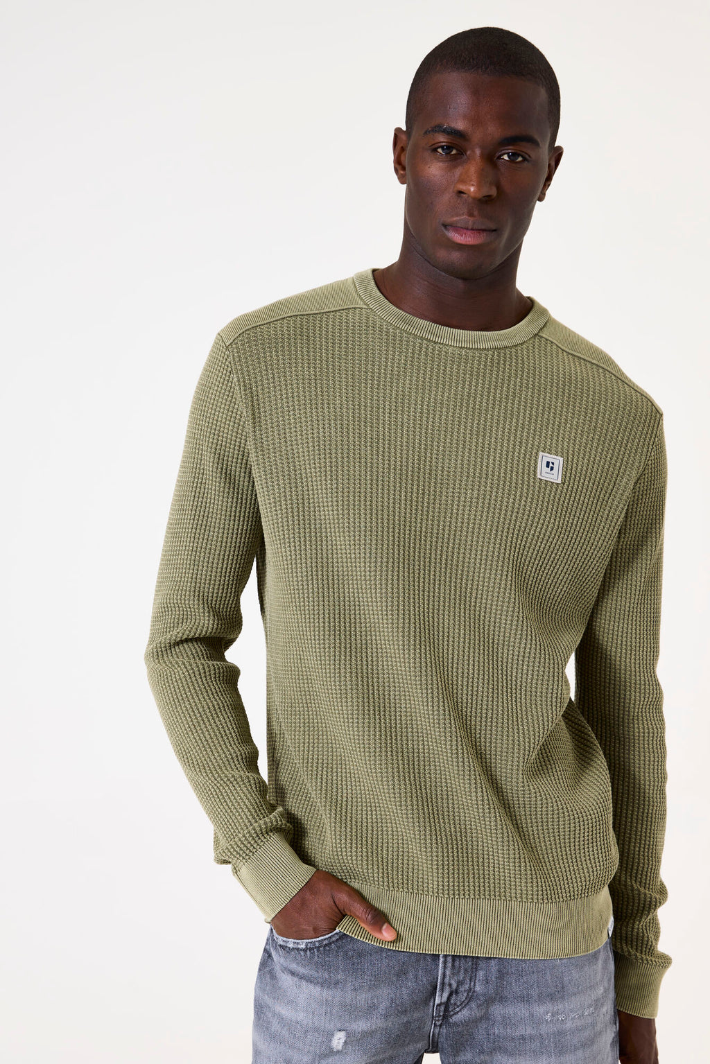 Man wearing a green textured sweater with a small logo on a white background