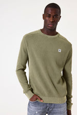 Load image into Gallery viewer, Man wearing a green textured sweater with a small logo on a white background
